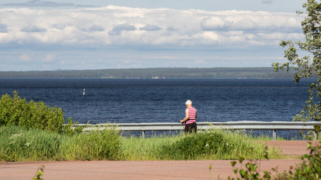 old woman practicing Nordic walking on a lakeshore