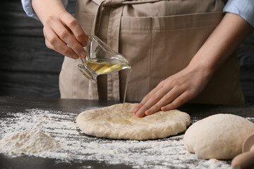 Female chef pouring oil onto raw dough on table, closeup