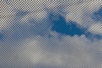 Black grid with square cells against a blue sky with white clouds, bottom view.