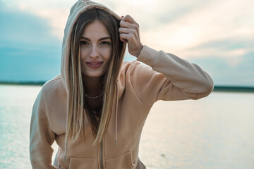 portrait of a beautiful girl in a jacket and hood on the beach against the background of a beautiful sunset