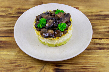 Tasty layered salad with roasted mushrooms, potato, eggs, cheese and mayonnaise on wooden table