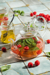 Hot raspberry tea in transparent teapot on a stone table. Fresh berries, mint, glass cup