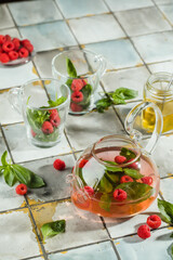Hot raspberry tea in transparent teapot on a stone table. Fresh berries, mint, glass cup