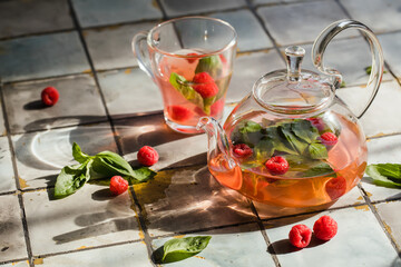 Hot raspberry tea in transparent teapot on a stone table. Fresh berries, mint, glass cup