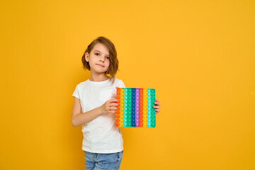 little girl holding pop it antistress toy on yellow background