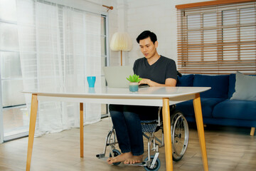 Asian handicapped man in a wheelchair uses his abilities to efficiently work on a laptop computer...