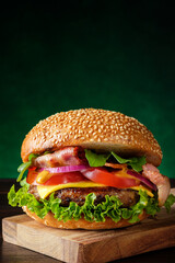 Fresh delicious burger on dark green background with copy space, vertical composition. Fast food concept.