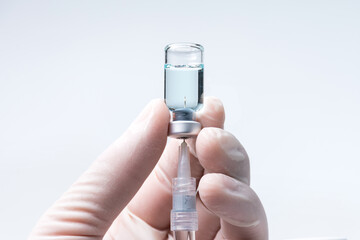 Doctor hand wears white medical glove holding flu, covid-19 liquid vaccine vial bottle and syringe are filling for preparing injection. Vaccination for fight Covid-19 virus concept.