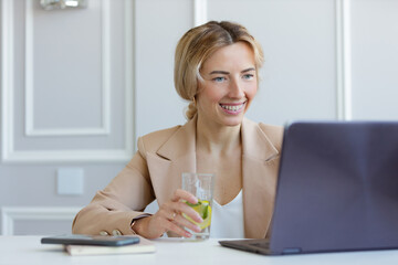 Portrait of a business woman in a suit working on a laptop and drinking lemonade 