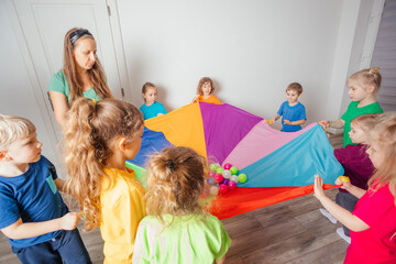 Teacher and kindergarten kids playing with colorful parachute