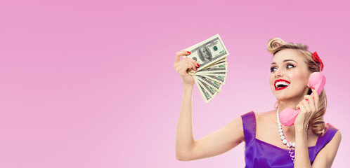 Image of Happy woman holding money, talk on phone, dressed in pinup style dress in polka dot, on...