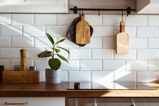 Kitchen brass utensils, chef accessories. Hanging kitchen with white tiles wall and wood tabletop.Green plant on kitchen background early morning light