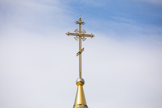 The golden dome and the cross of the Orthodox church against the blue sky and clouds.