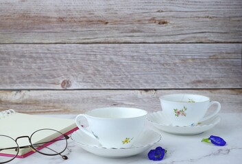 tea mug with glasses and a notebook with a pen rests on a marble table with a wooden background