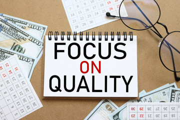 FOCUS ON QUALITY. text on white notepad paper near calendar on wood craft background