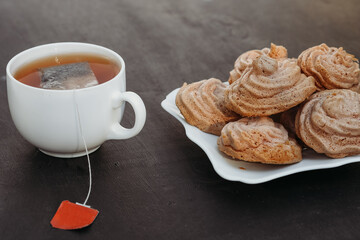 A cup of hot tea and biscuits close-up on a gray background. A sachet with a blank red label.