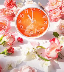 Orange round analog alarm clock on white background with rose buds. Summer morning concept. Eleven o'clock