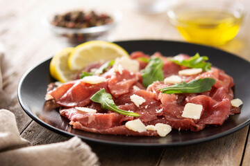 Marbled beef carpaccio on black plate and rustic wooden table. 
