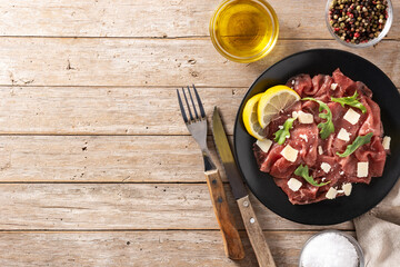 Marbled beef carpaccio on black plate and rustic wooden table. Top view. Copy space