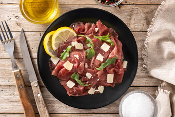 Marbled beef carpaccio on black plate and rustic wooden table. Top view. 