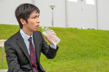 公園で水を飲むスーツ姿のビジネスマン