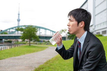 公園で水を飲むスーツ姿のビジネスマン
