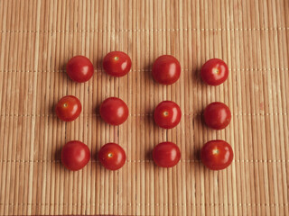 Small red tomatoes are arranged in a row on a cane napkin. Cherry tomatoes. 