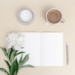 Top view of notebook, white peony flower, cup of cofffee on table. Creative workspace minimal style with aroma candle for comfort work