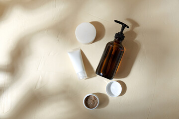 beauty, cosmetics and object concept - bottle of shower gel, soap, body scrub and moisurizer on beige surface with sgadows