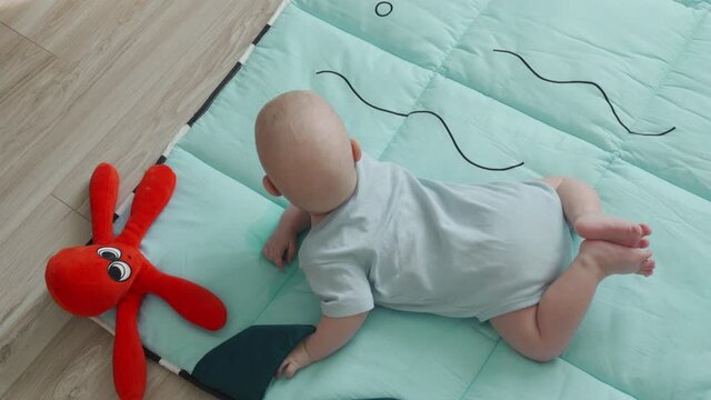 Tummy time for babies, baby learn head control, 3 month old baby boy lifting head lying on tummy on activity play mat at home. High quality 4k footage