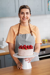 culinary, baking and cooking food concept - happy smiling young woman with raspberry cake on kitchen at home