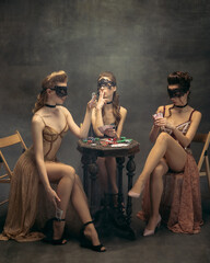 Pretty women in vintage 20s dresses. Young girls in art action sitting together and posing on wall...