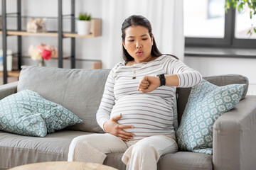 pregnancy, rest, people and expectation concept - pregnant asian woman with smart watch having...