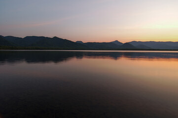 Fototapeta na wymiar 夕暮れの空に際立つ山々のシルエットを湖面に反射する湖。