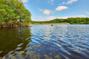 Two people kneeling on a paddleboard in a reservoir with blue sky and trees in the background