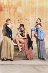 Pretty women in vintage 20s dresses. Young girls in art action sitting together and posing on wall background.