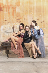 Pretty women in vintage 20s dresses. Young girls in art action sitting together and posing on wall background.