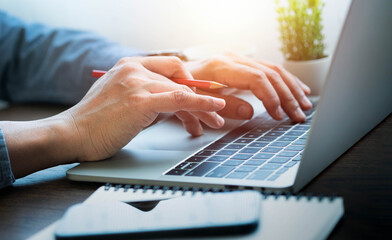 Close-up of man hands using and typing keyboard of laptop computer on office desk. Workspace,...
