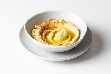 Chickpea hummus  white bowl with olive oil and paprika on white background.