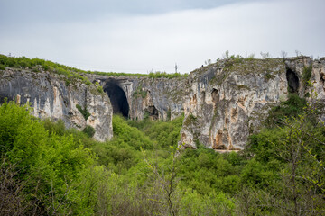 Fototapeta na wymiar The huge entrance of Prohodna cave as seen from far away. Northern Bulgaria, Beauty in Nature