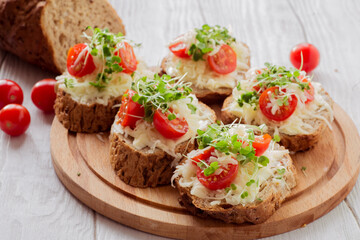 Bruschetta with tomatoes, cheese and microgreens on a board.