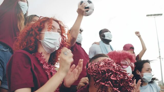 Multiracial sport fans with protective face mask watching sport event in football stadium arena. Competition, games and sport in times of covid