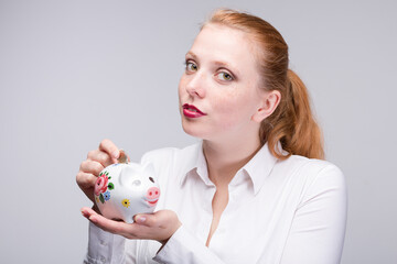 Fototapeta na wymiar Young woman feed her piggy bank / porcelain bank with a coin