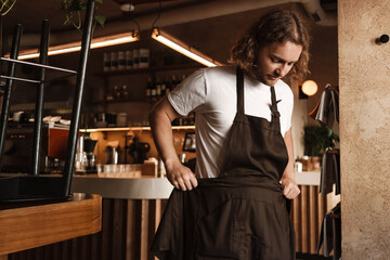 Young white cafe worker in apron standing indoors