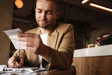 Young white man working with receipt while sitting at table in cafe