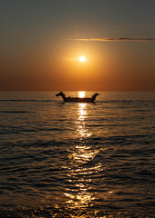 silhouette of a dragon boat at sunset in the sea in summer