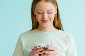 Young blonde woman smiling and using mobile phone