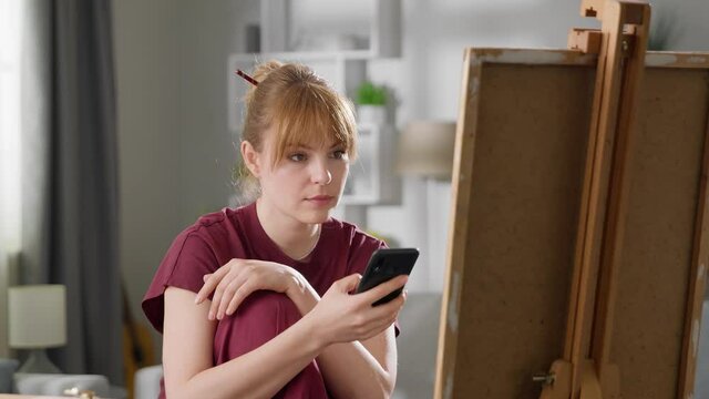 Young attractive woman learns to draw using video lesson on mobile phone.