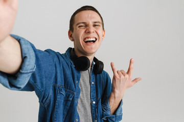 Young brunette man with headphones smiling and gesturing horns sign