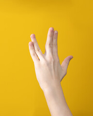 woman hand shows Vulcan salute on yellow background. Hand gesture that means Live long and prosper